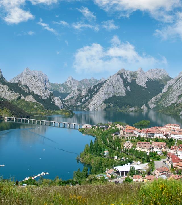 Vogelperspektive auf Riaño in Nordspanien. Der Ort liegt am Ufer eines großen Stausees, umgeben von grünen Hängen und schroffen Berggipfeln.