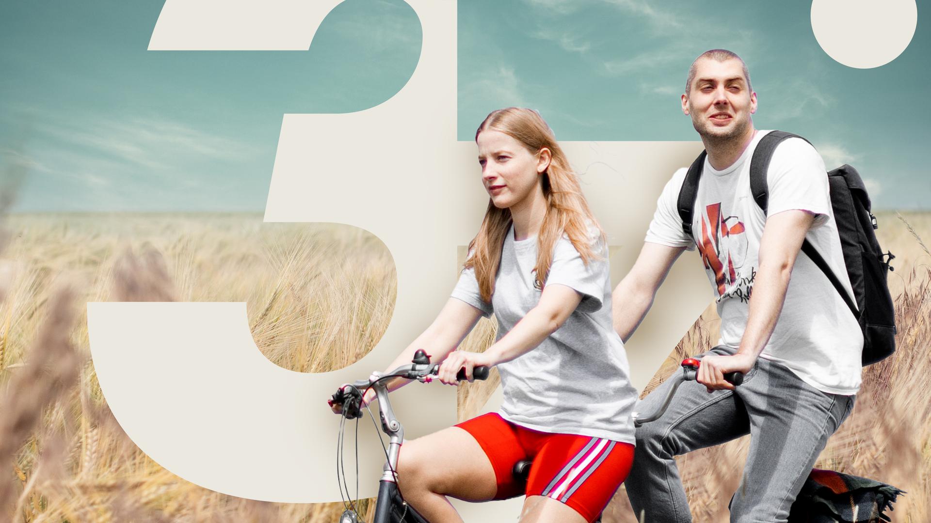 David und Cindy sitzen auf einem Tandem (Cindy vorn, David hinten) und fahren durch ein Feld, welches im Vordergrund zu sehen ist. Im Hintergrund sieht man einen bewölkten Himmel und ein Kornfeld.