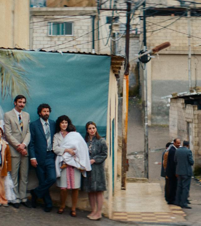 Ein Fotograf fotografiert eine Hochzeitsgesellschaft, die sich für das Bild in Reihen hintereinander aufgestellt hat.