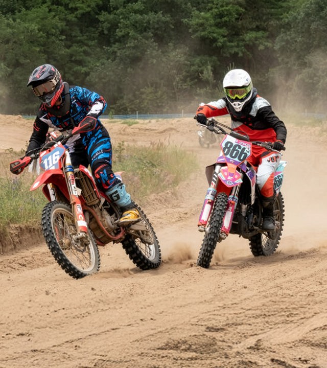 "SOKO Potsdam - Im toten Winkel": Auf einer staubigen Motocross-Strecke fahren zwei junge Fahrerinnen dicht nebeneinander durch eine Kurve. Links Sina Götz, rechts Melis Seyhan – beide in voller Schutzkleidung, mit Helm und Schutzbrille. Ihre Maschinen schleudern Sand auf, die Räder graben sich tief in den Boden.