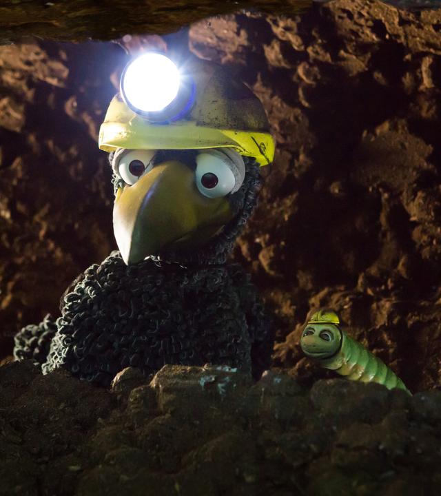 Rabe Rudi und Wurm Lotti sitzen in Gretes Tunnel. Rudi hat eine Stirnlampe auf.