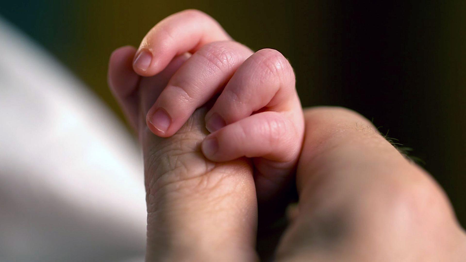 Hand einer Frau hält Händchen von Säugling.