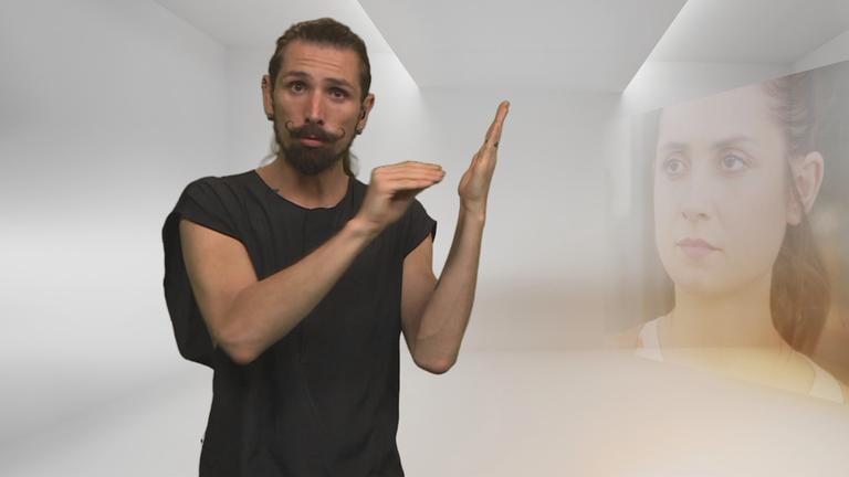 Gebärdendolmetscher Eyk Kauly steht vor hellem, neutralem Hintergrund und führt eine Gebärde mit beiden Händen aus. Rechts im Bild ist leicht transparent das Gesicht einer Frau eingeblendet, das als inhaltlicher Bezug zur Übersetzung wirkt.