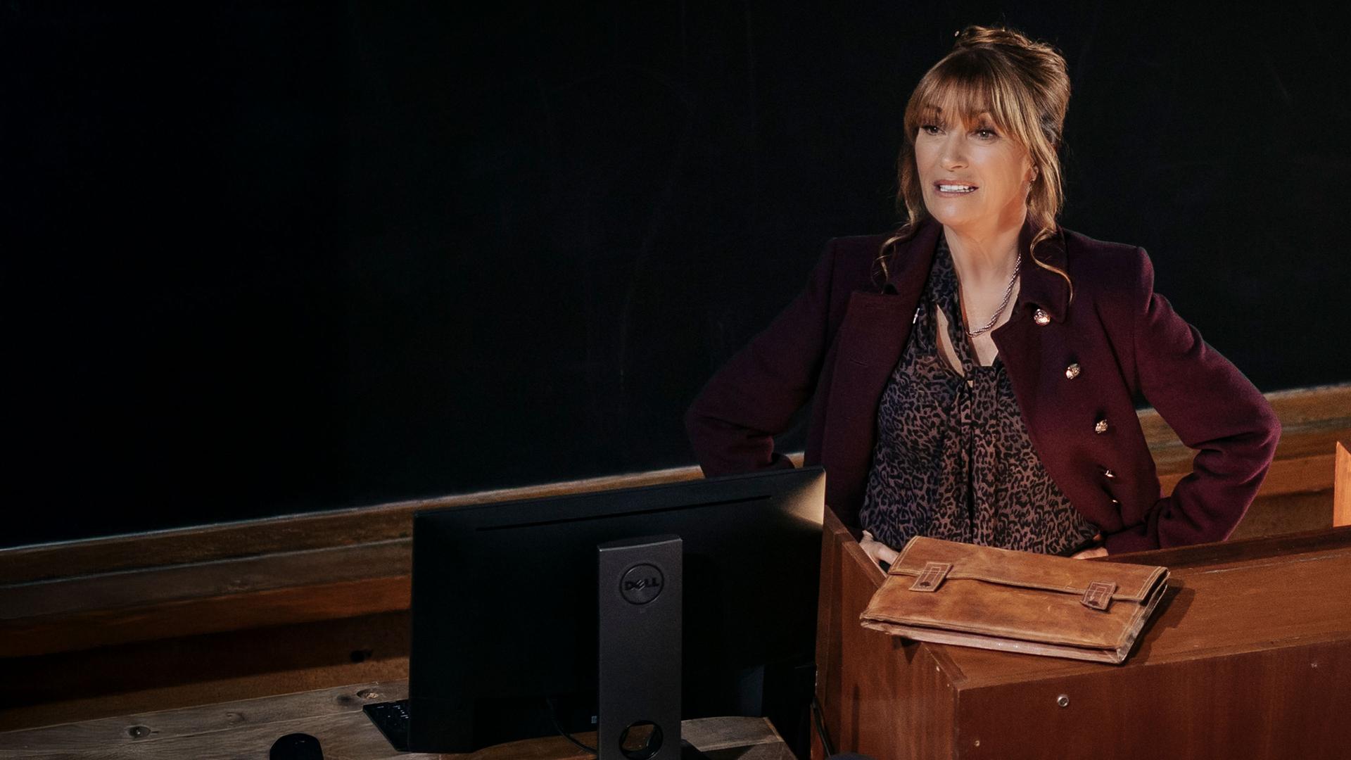 "Harry Wild - Mörderjagd in Dublin: Immer Ärger mit Harry": Harry Wild (Jane Seymour) steht vor einer Tafel an einem Rednerpult in einem Universitätshörsaal und spricht nach links blickend.