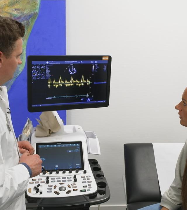 Patientin und Arzt stehen vor einem EKG