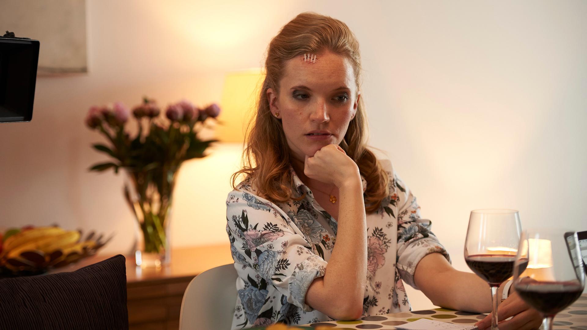 "Cecelia Ahern: In deinem Leben - Teil 1": Joyce sitzt an einem Tisch und schaut nachdenklich auf die Tischdecke vor ihr. Vor ihr steht ein halb gefülltes Rotweinglas, sie hat den rechten Ellbogen auf den Tisch gestützt und die Hand zu einer Faust gemacht, mit der sie das Kinn stützt.