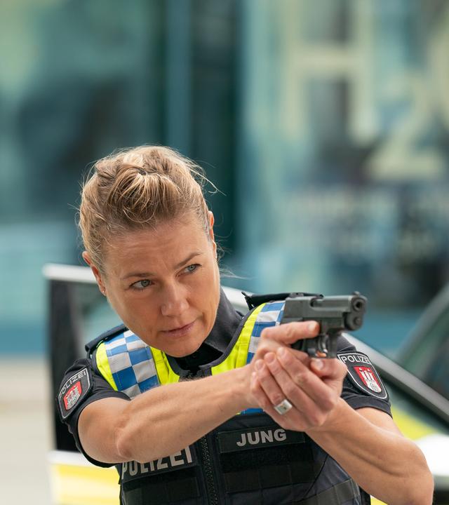 Der Polizist Nick Brandt (Raúl Richter) und seine Kollegin Franzi Jung (Rhea Harder-Vennewald) stehen nebeneinander. Beide zielen mit ihrer Waffe in die gleiche Richtung.