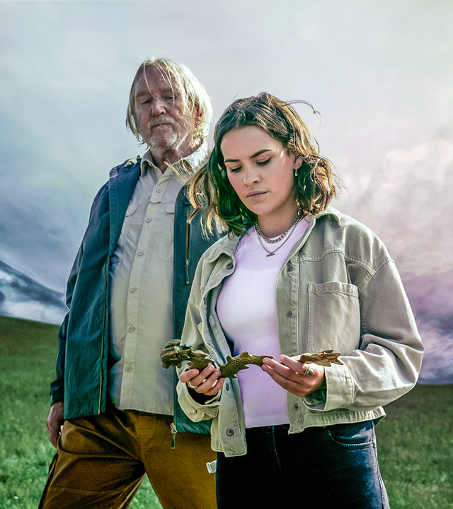 Issie steht neben ihrem Großvater Gordon, der mit starren Blick auf die goldene Drachenfigur schaut, die Issie in ihren Händen hält. Um sie herum beginnt ein Unwetter aufzuziehen.