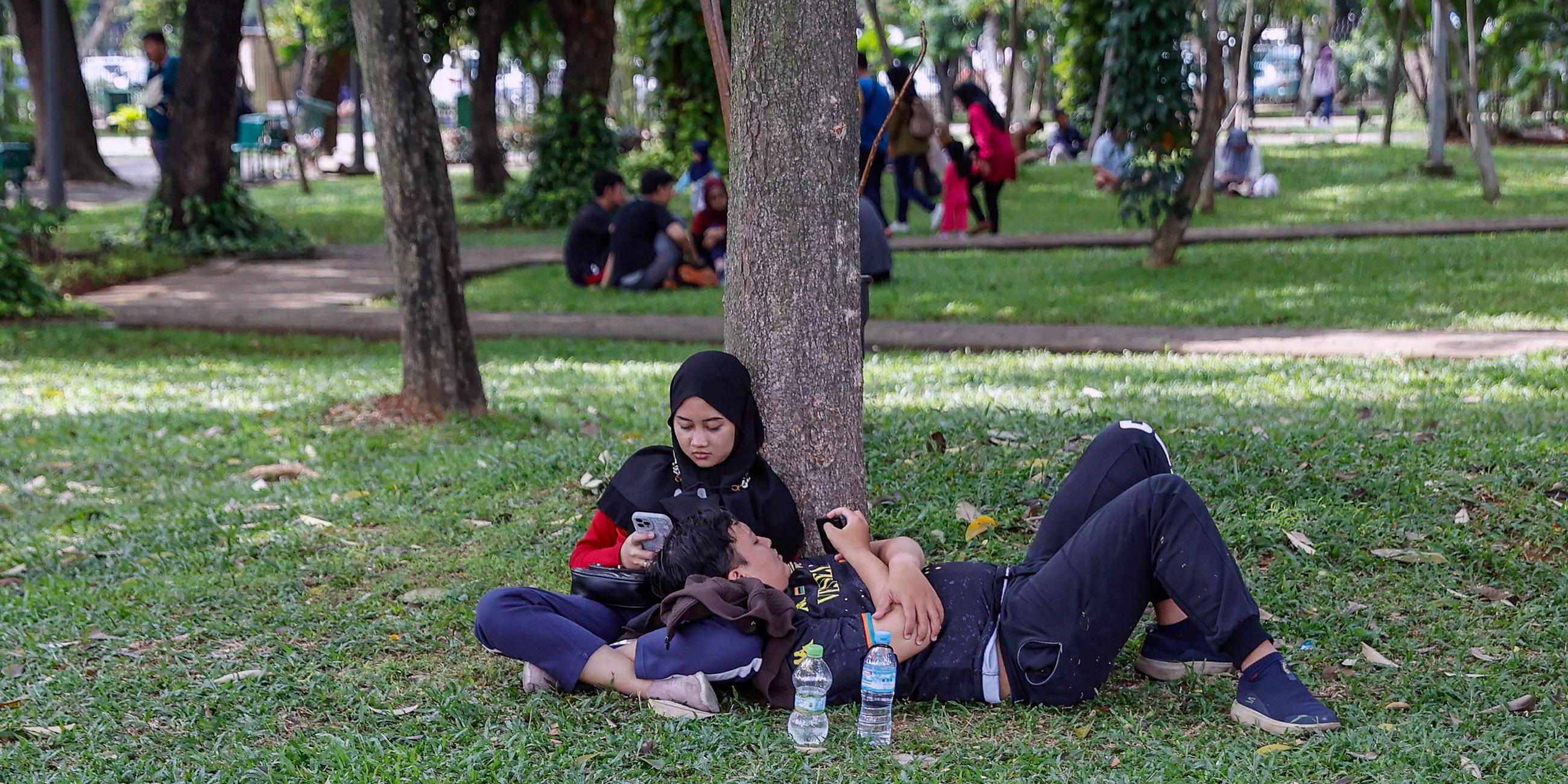 Ein Paar sitzt auf dem Rasen in einem öffentlichen Park in Jakarta (Indonesien), aufgenommen am 04.12.2022