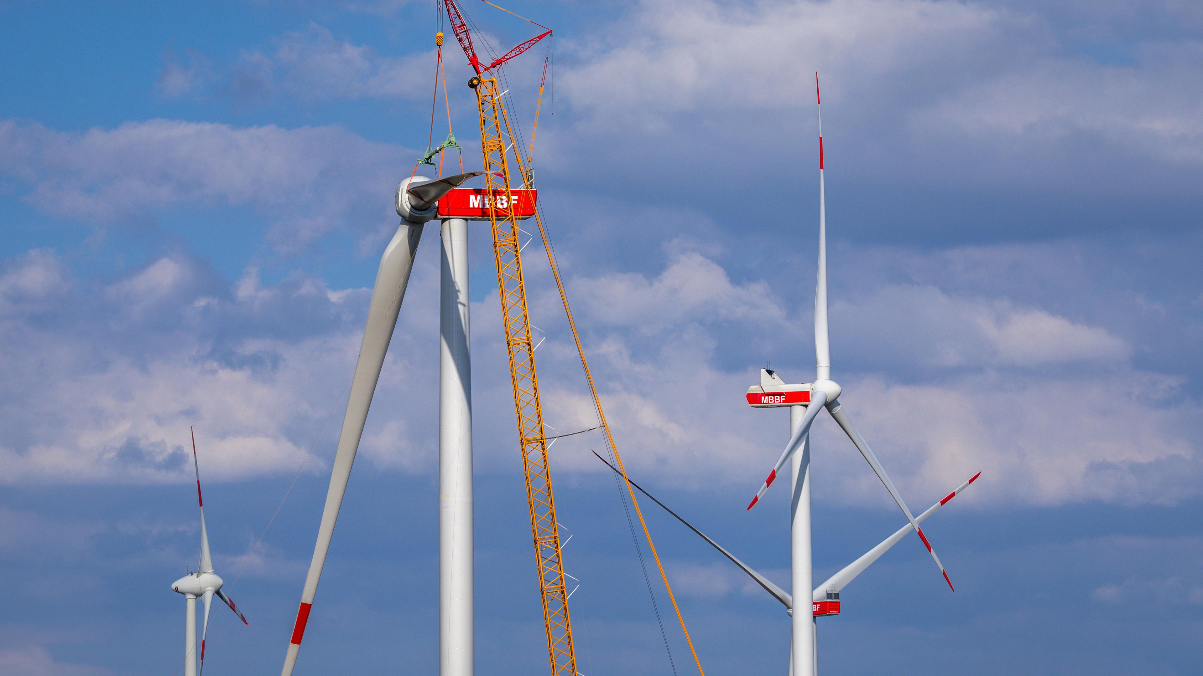 Ein Kran hebt auf der Baustelle eines neuen Windparks ein Rotorblatt für die Montage an das Generatorhaus. 