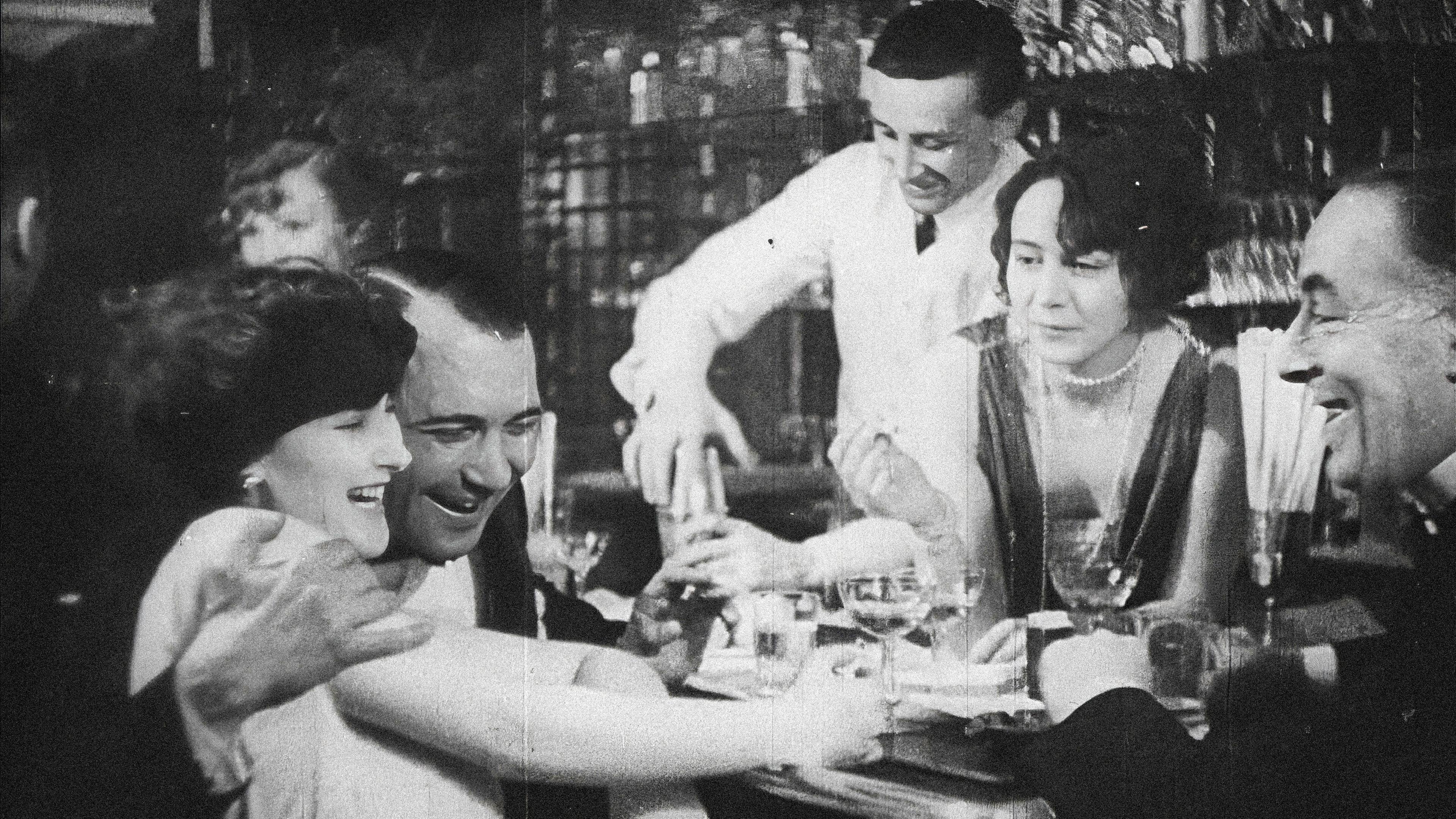 An einer Bar sitzt links im Bild ein Mann, der seinen Arm um eine Frau legt. Sie lacht. Rechts davon sitzen ein Mann und eine Frau, die sich ebenfalls amüsieren. Im Hintergrund schenkt ein Barkeeper ein Getränk ein.