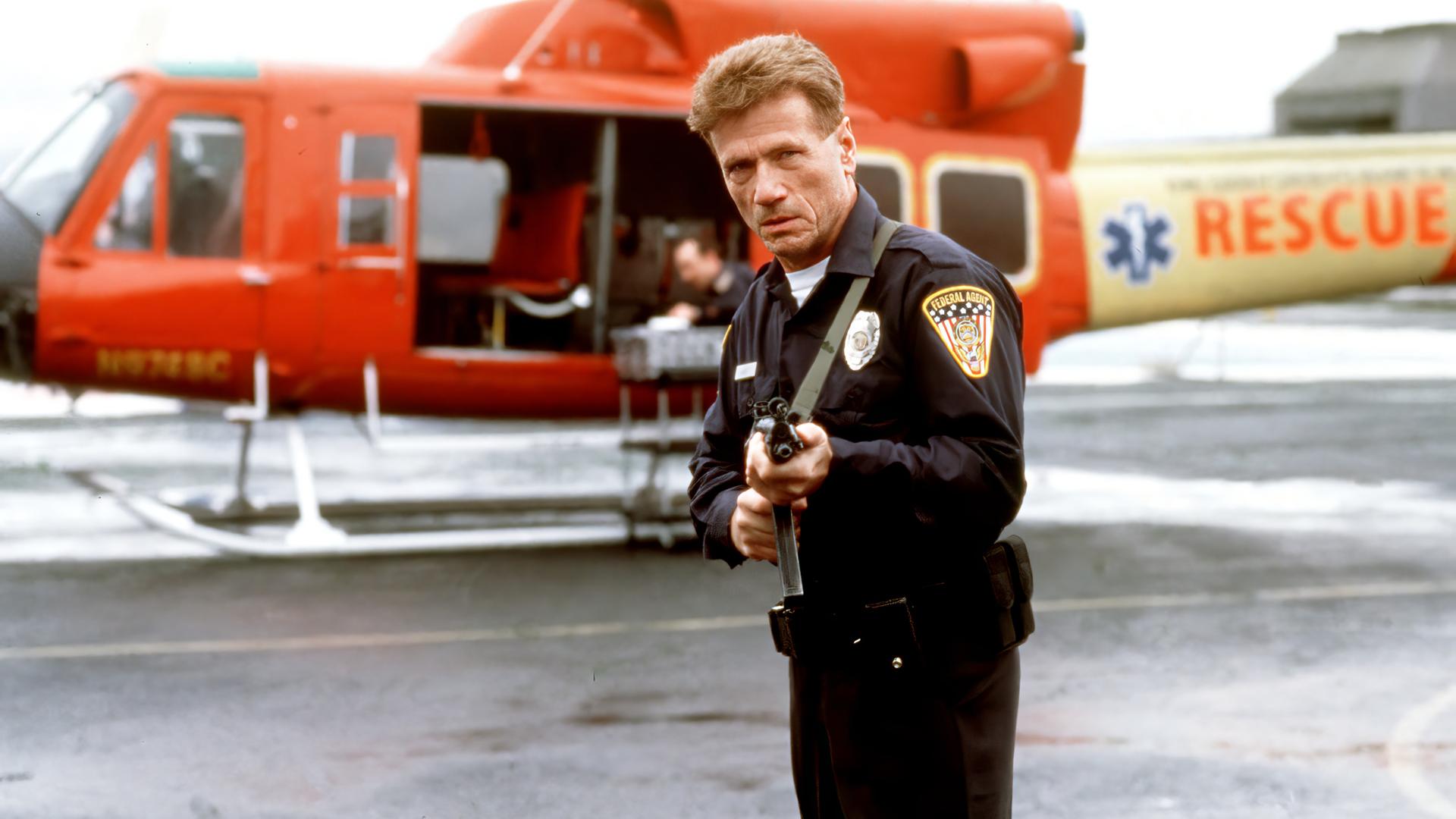 Quentin Darby (Jürgen Prochnow) steht mit einer Waffe neben einem kleinen Flugzeug