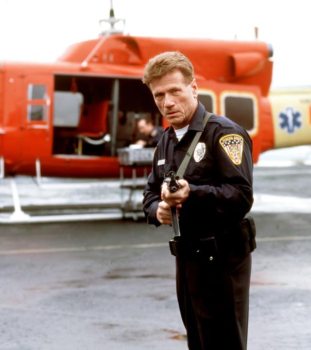 Quentin Darby (Jürgen Prochnow) steht mit einer Waffe neben einem kleinen Flugzeug