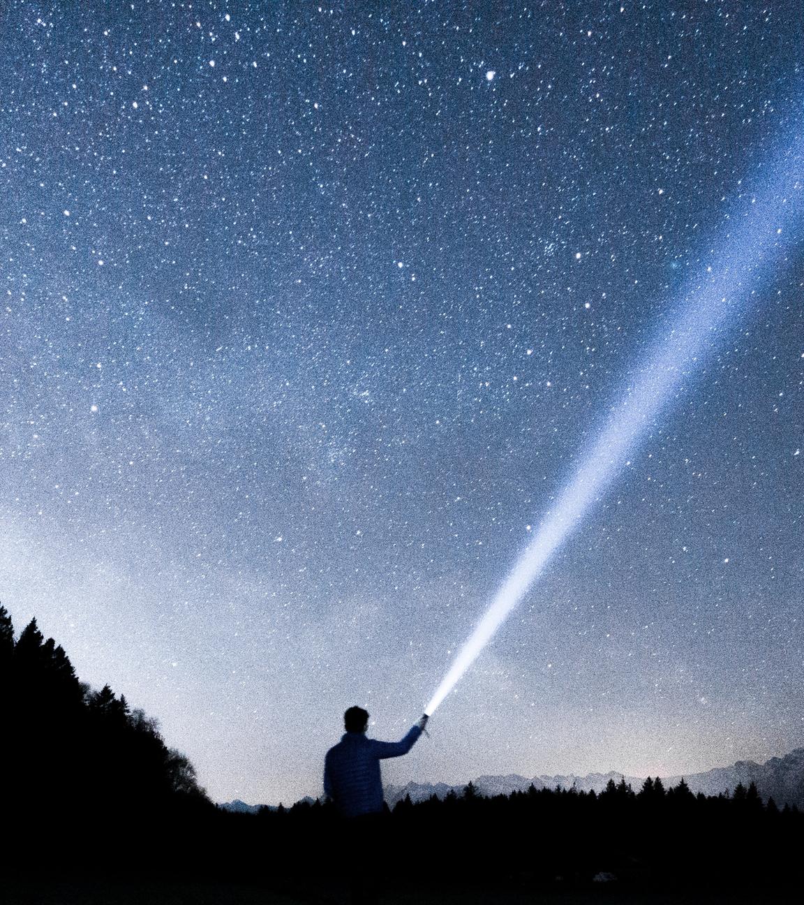 Ein Mensch leuchtet mit einer Taschenlampe in den Sternenhimmel.