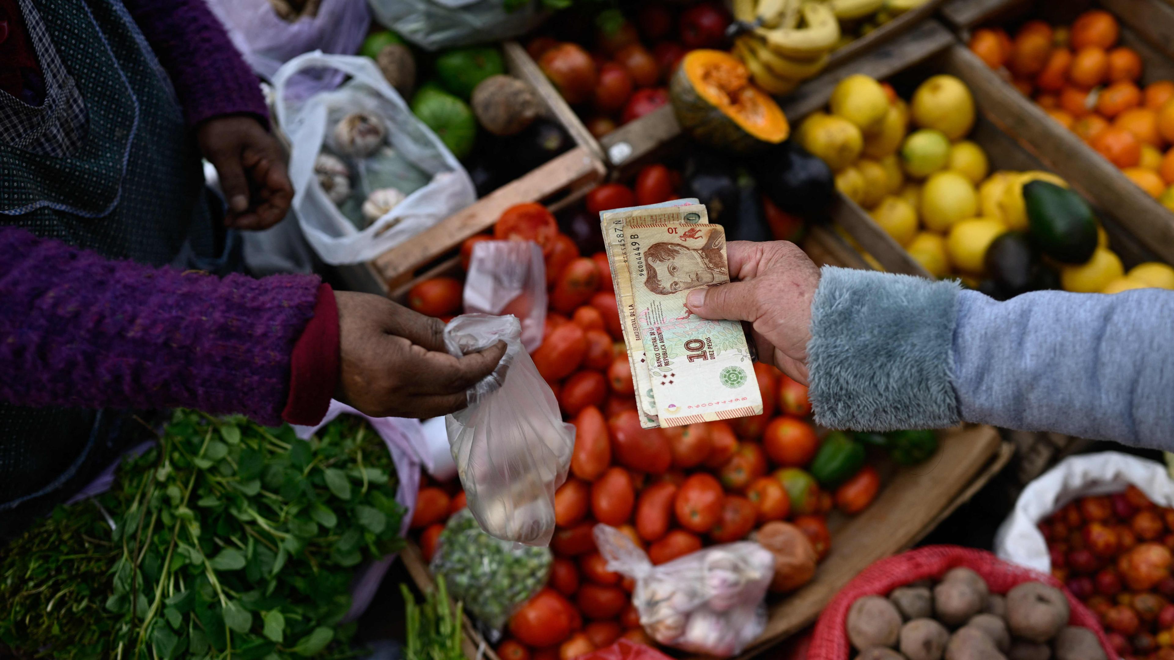 Eine Person überreicht Pesos an eine andere Person an einem Marktstand in Buenos Aires.