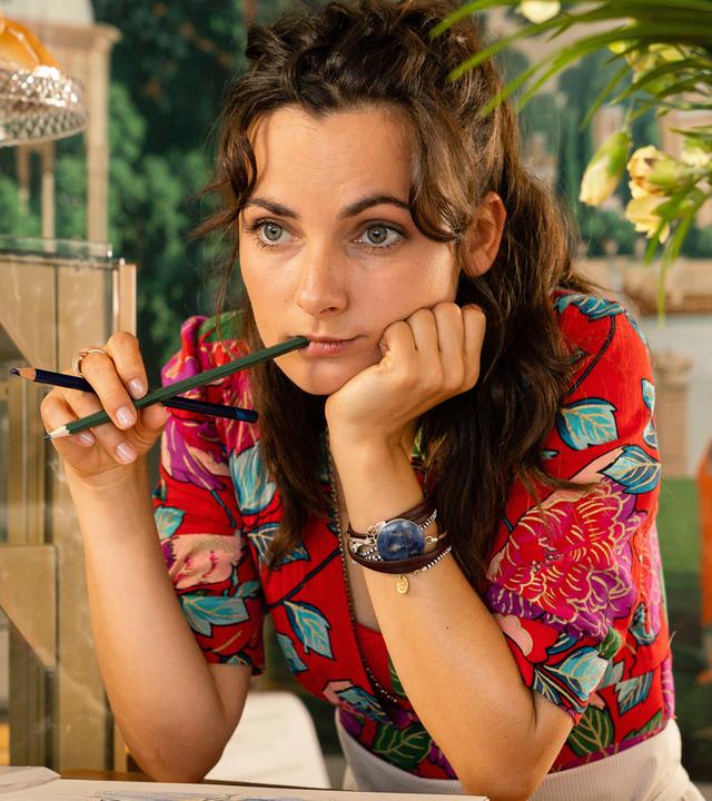 Jette (Paula Schramm), mit beiden Ellenbogen auf dem Tisch im Cafè abgestützt und einen Bleistift am Mund, träumt vor sich hin.