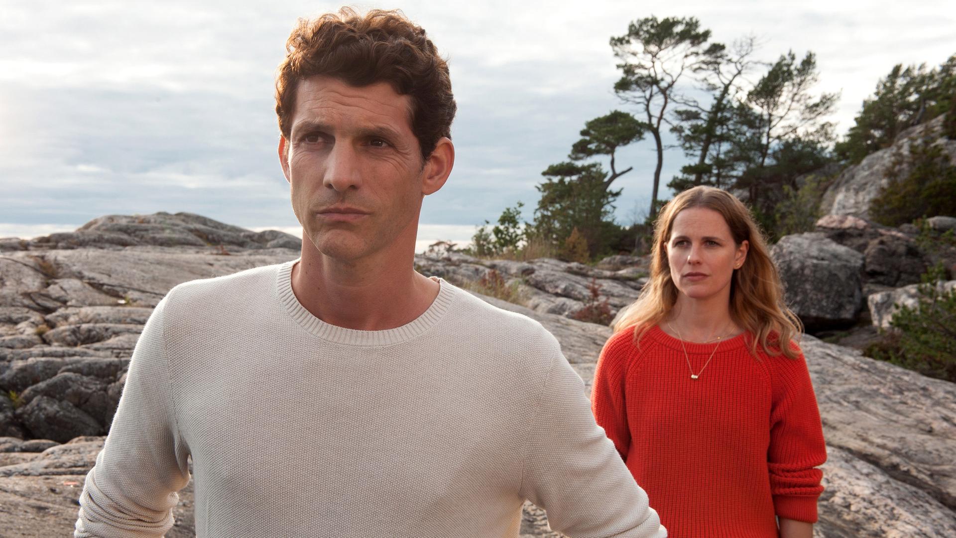 "Inga Lindström - Heimkehr": Lennard (Martin Bretschneider) und Ellen (Isabell Polak) stehen hintereinander auf Felsen. Ellen steht im Rücken von Lennard und beide schauen besorgt.