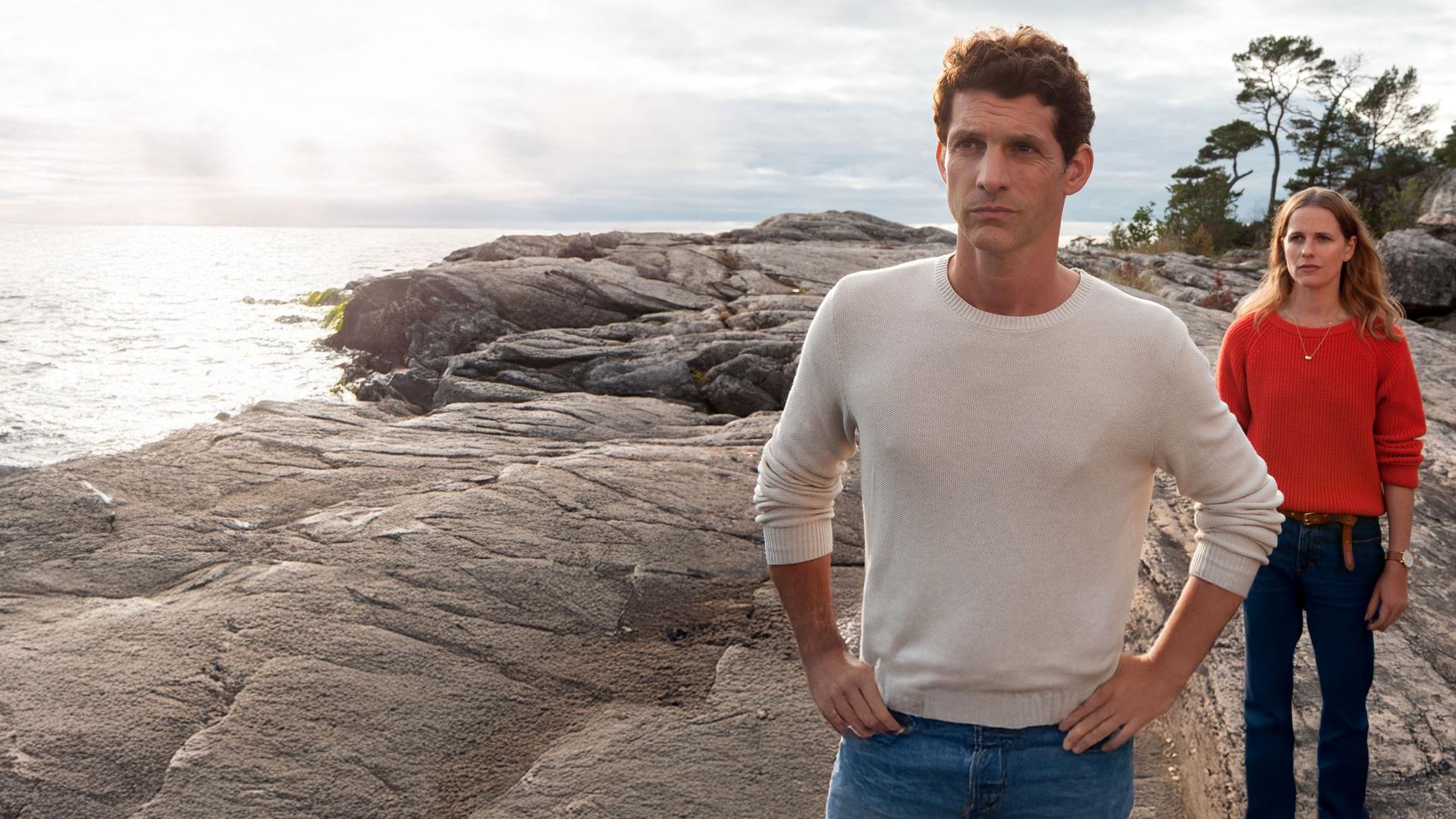 "Inga Lindström - Heimkehr": Lennard (Martin Bretschneider) und Ellen (Isabell Polak) stehen hintereinander auf Felsen. Ellen steht im Rücken von Lennard und beide schauen besorgt.