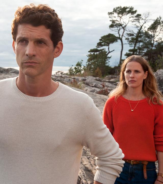 "Inga Lindström - Heimkehr": Lennard (Martin Bretschneider) und Ellen (Isabell Polak) stehen hintereinander auf Felsen. Ellen steht im Rücken von Lennard und beide schauen besorgt.
