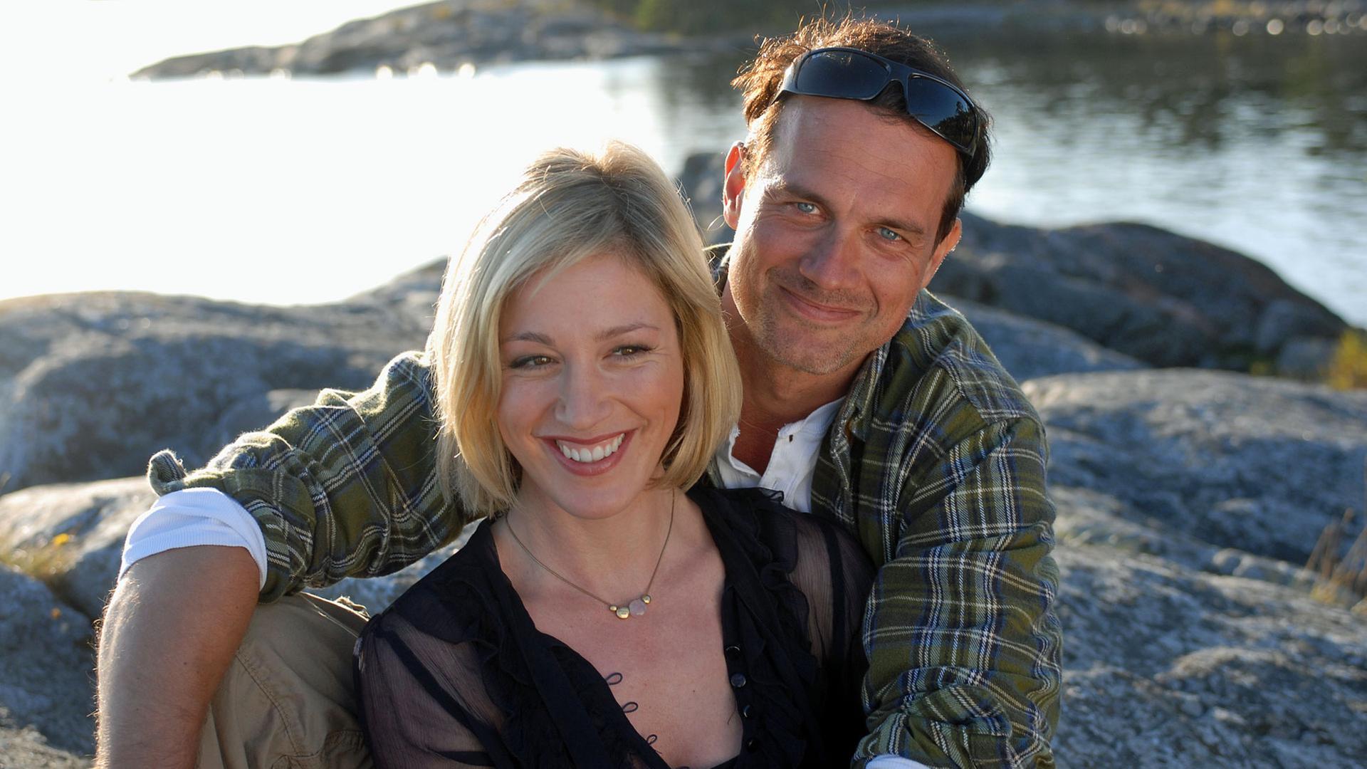 "Inga Lindström: Mein falscher Verlobter": Nina (Julia Stinshoff) und Jonas (Ralf Bauer) sitzen umarmt auf einem Felsen an einer Küste.