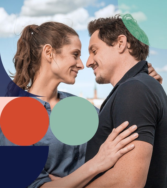 "Inga Lindström: Verliebt in meinen Chef": Anna Lund (Ellenie Salvo Gonzalez) und Sven Berggren (Markus Brandl) umarmen sich und schauen sich dabei an. Im Hintergrund: Wasser, Häuser und Stockholmer Stadtlandschaft.