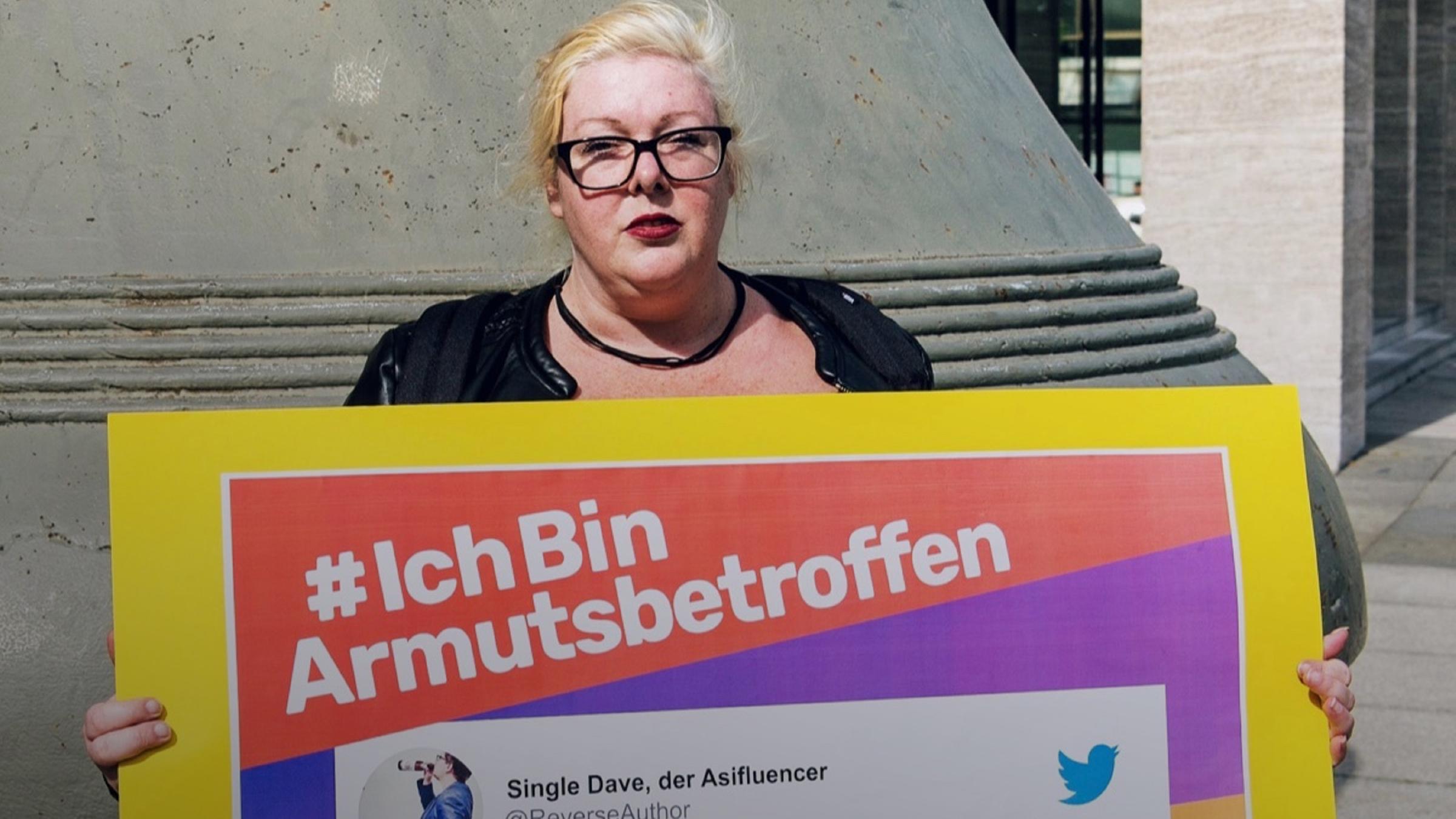 Anni W. hät ein Schild hoch mit der Aufschrift "#IchBinArmutsbetroffen"