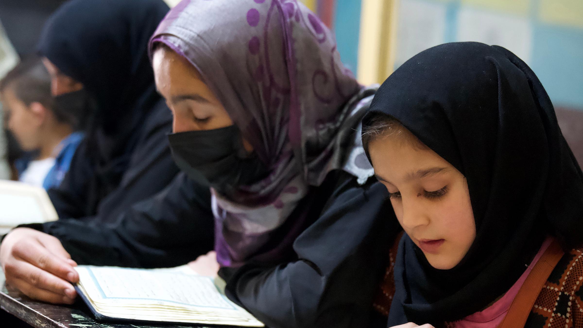 Drei Mädchen sitzen in der Koranschule an einem Tisch und lesen den Koran.