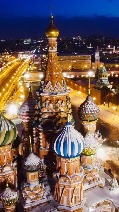 Luftbild: Moskau bei Nacht mit beleuchteten Straßen und einer Kathedrale mit bunten Türmen im Vordergrund