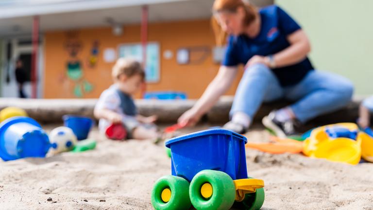 Eine Erzieherin spielt mit einem Kind im Sandkasten einer Kita.