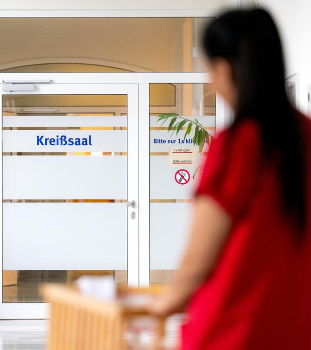 Eine Hebamme schiebt ein Bett mit einem Säugling zum Kreißsaal.