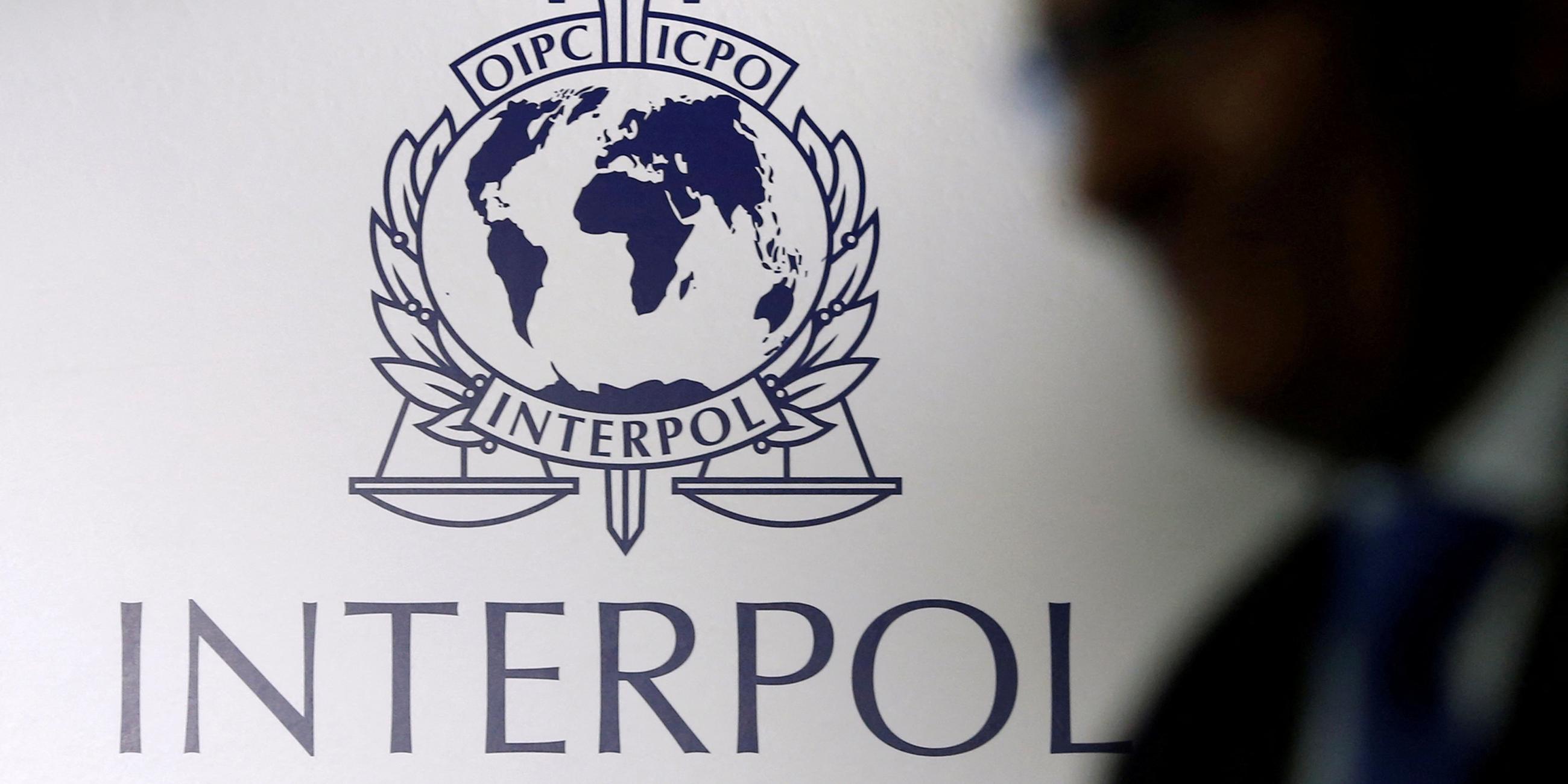 Ein Schatten eines Mannes vor einem Interpol-Logo