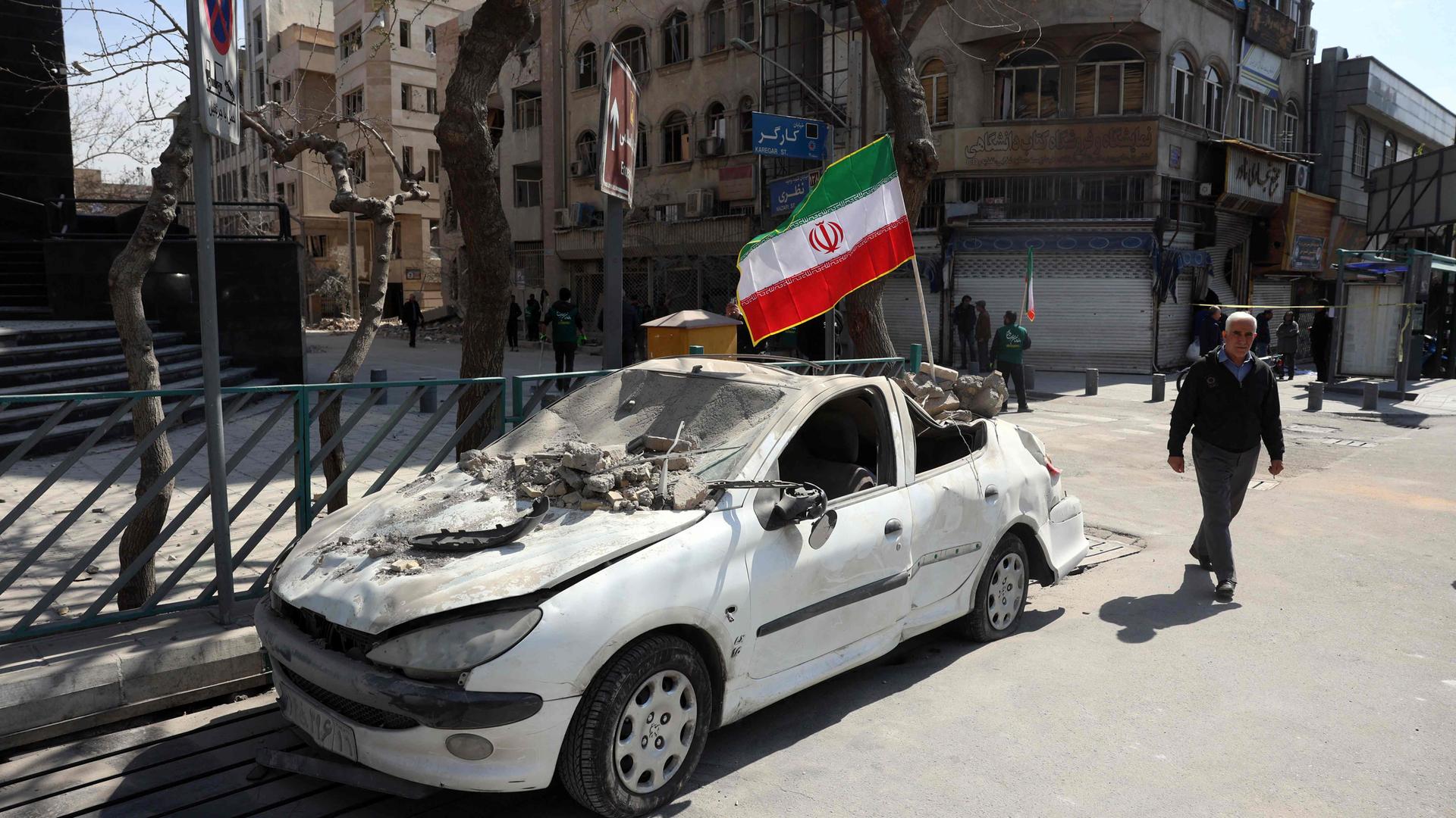 Mann läuft an einem von US-Angriff zerstörten Auto in Teheran vorbei.