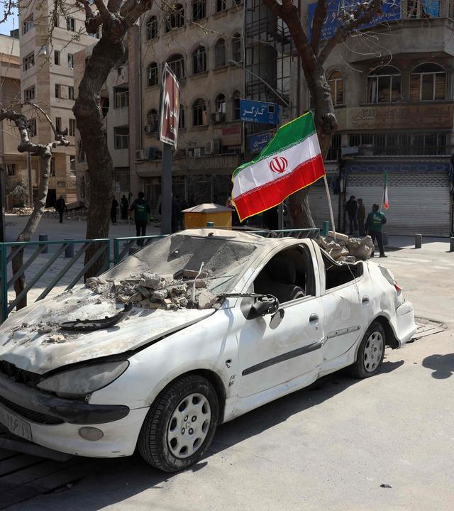 Mann läuft an einem von US-Angriff zerstörten Auto in Teheran vorbei.