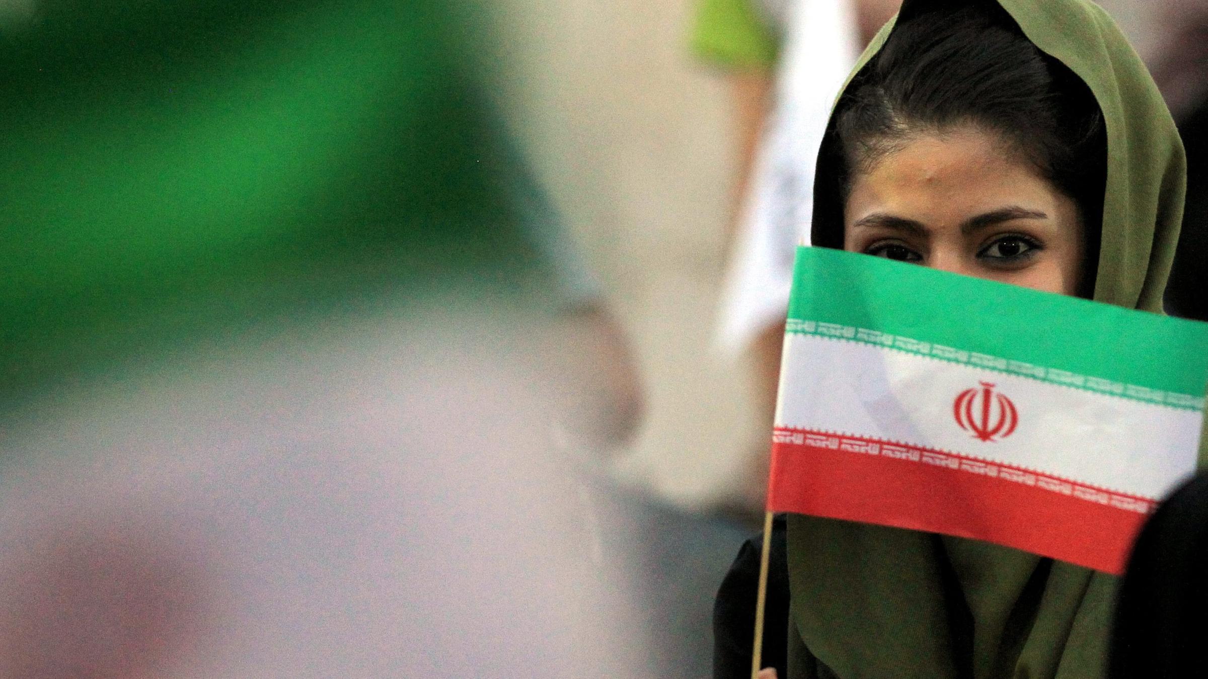 Eine iranische Frau hält sich eine Flagge vors Gesicht.