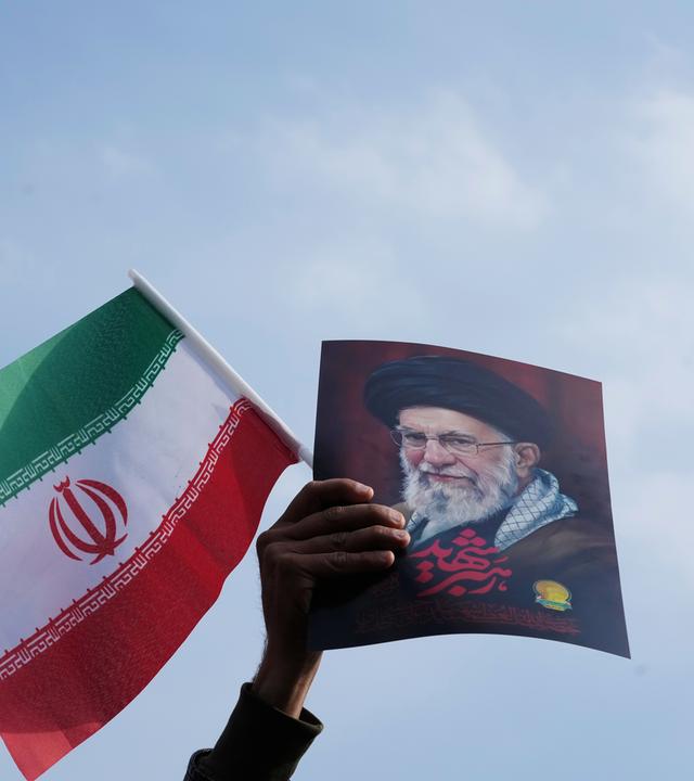 Eine Hand hält eine iranische Flagge und ein Bild vom getöteten iranischen Führer Ajatollah Ali Chamenei hoch.