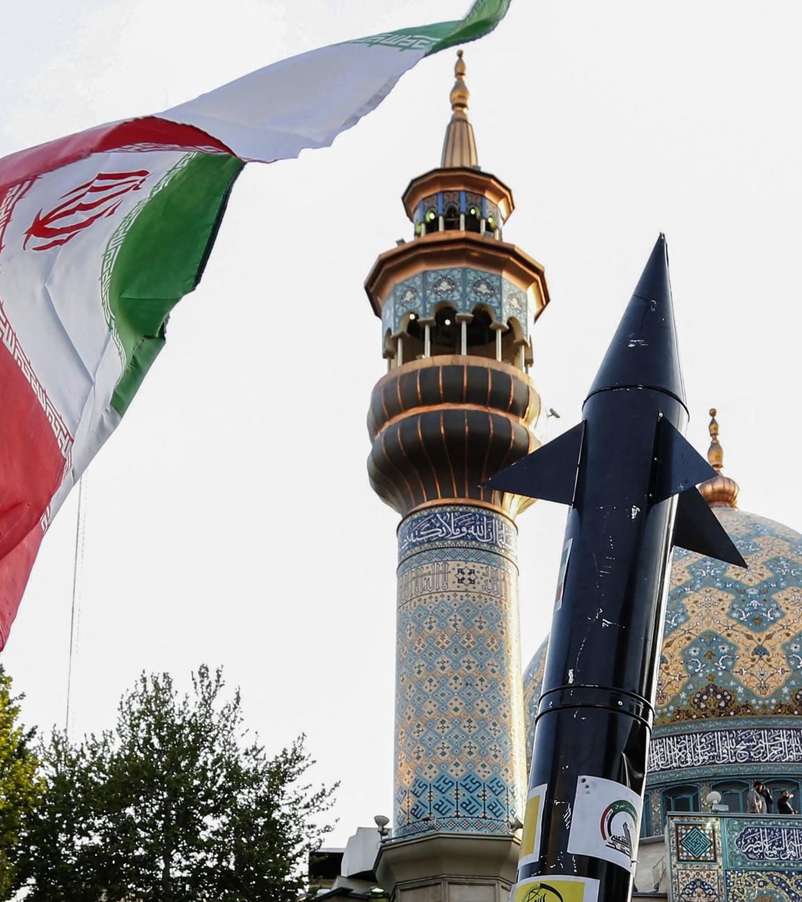 Iraner heben eine Flagge und die Attrappe einer Rakete während einer Feier nach dem iranischen Raketen- und Drohnenangriff auf Israel am 15. April 2024 auf dem Palästina-Platz im Zentrum von Teheran. 