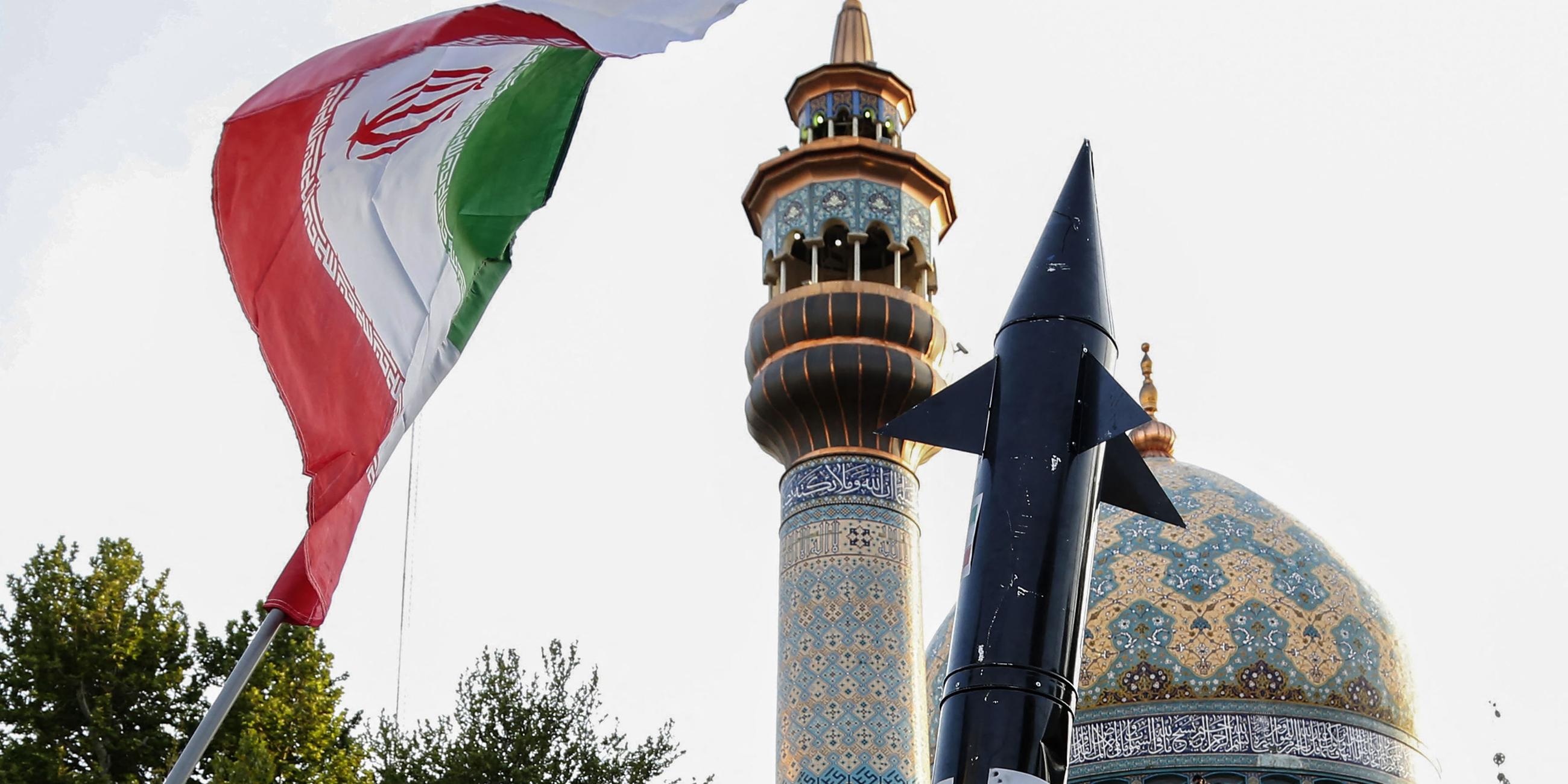 Iraner heben eine Flagge und die Attrappe einer Rakete während einer Feier nach dem iranischen Raketen- und Drohnenangriff auf Israel am 15. April 2024 auf dem Palästina-Platz im Zentrum von Teheran. 