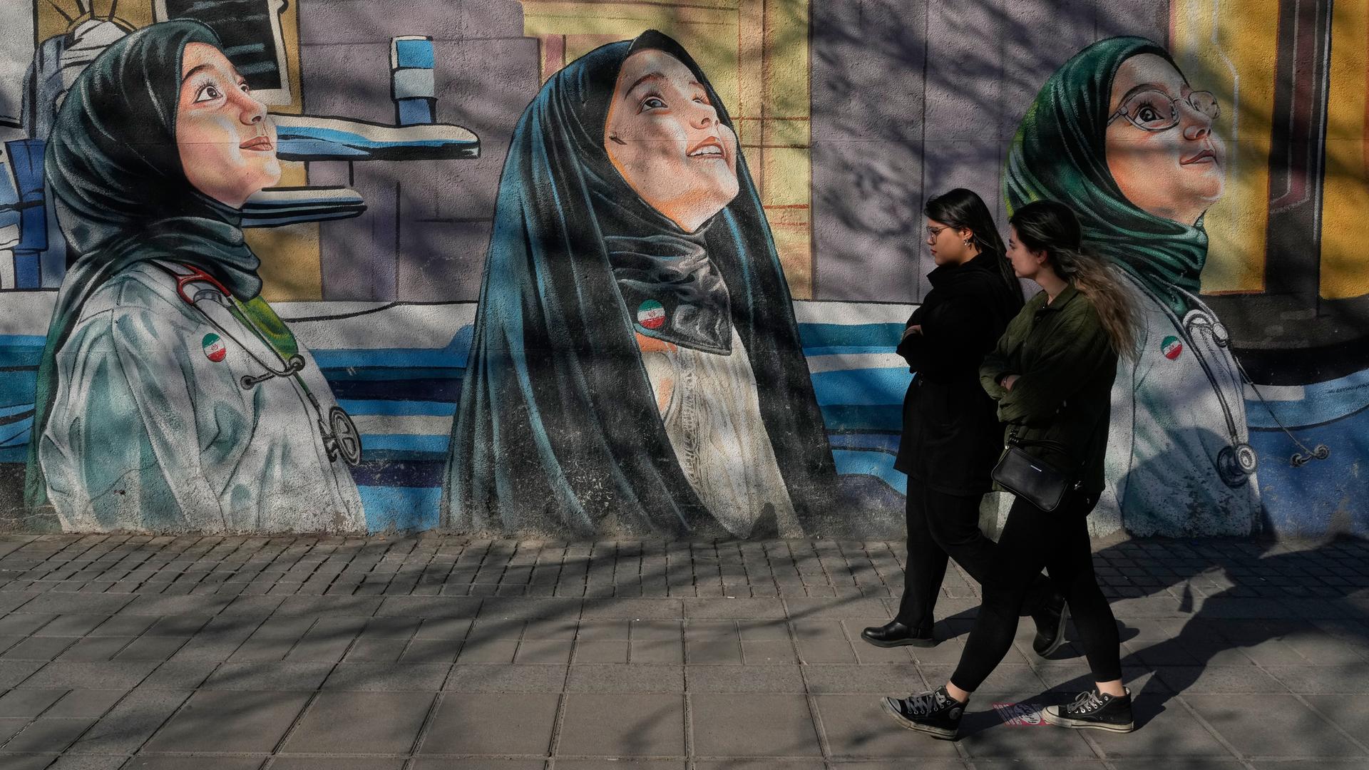 Frauen gehen an einem Gemälde an der Wand einer Mädchenschule im Zentrum von Teheran, Iran, vorbei. 