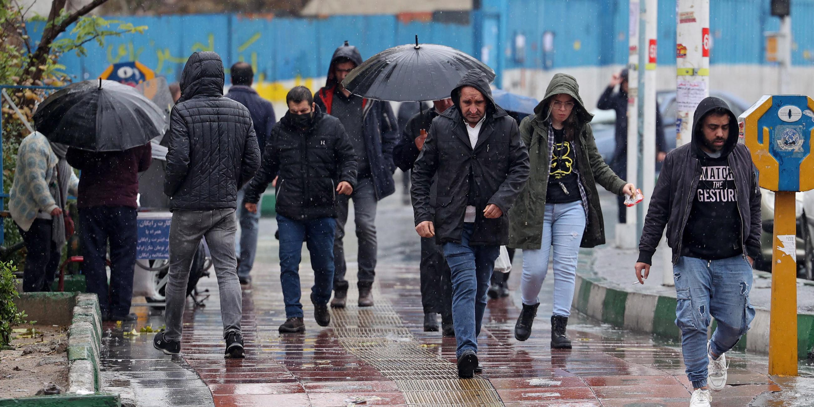 Menschen gehen an einem regnerischen Tag in Teheran auf einer Straße