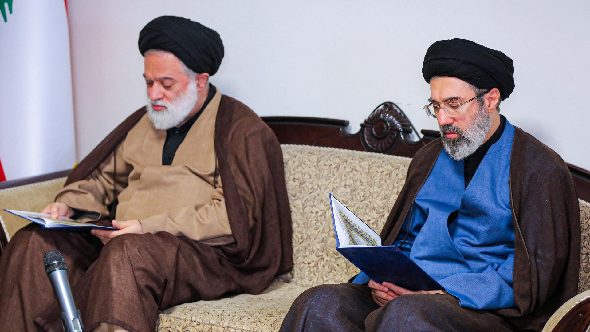 Modschtaba Chamenei sitzt auf einem Sofa und hält ein offenes Buch in der Hand.