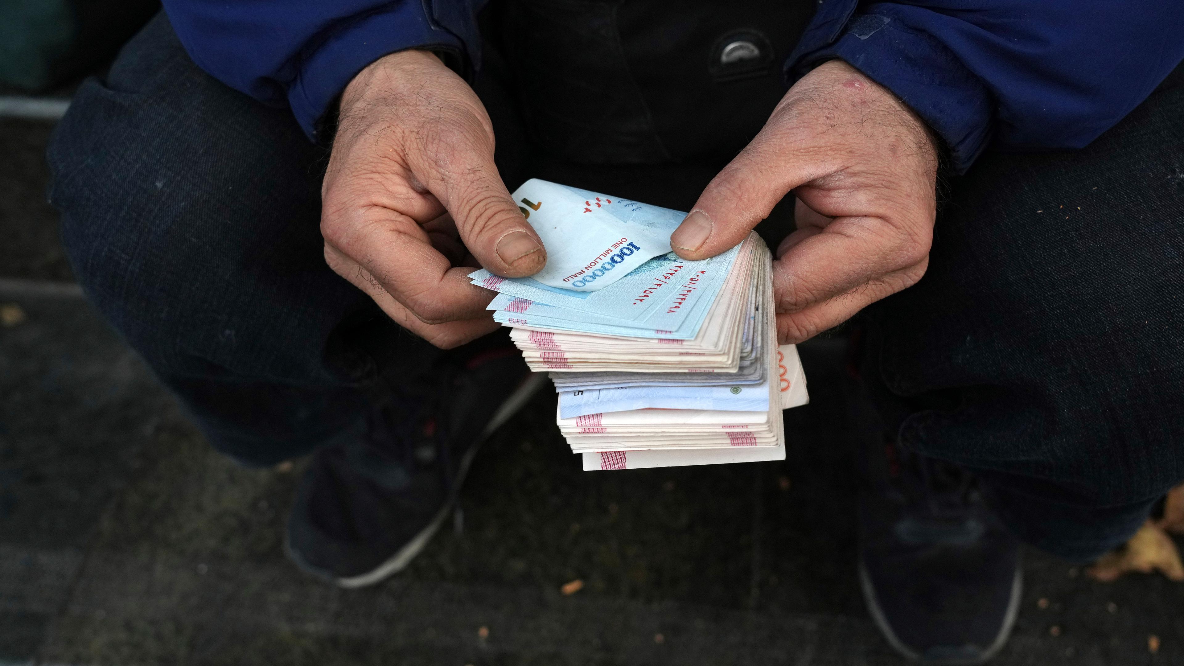 Ein Mann zählt Banknoten der iranischen Währung Rial