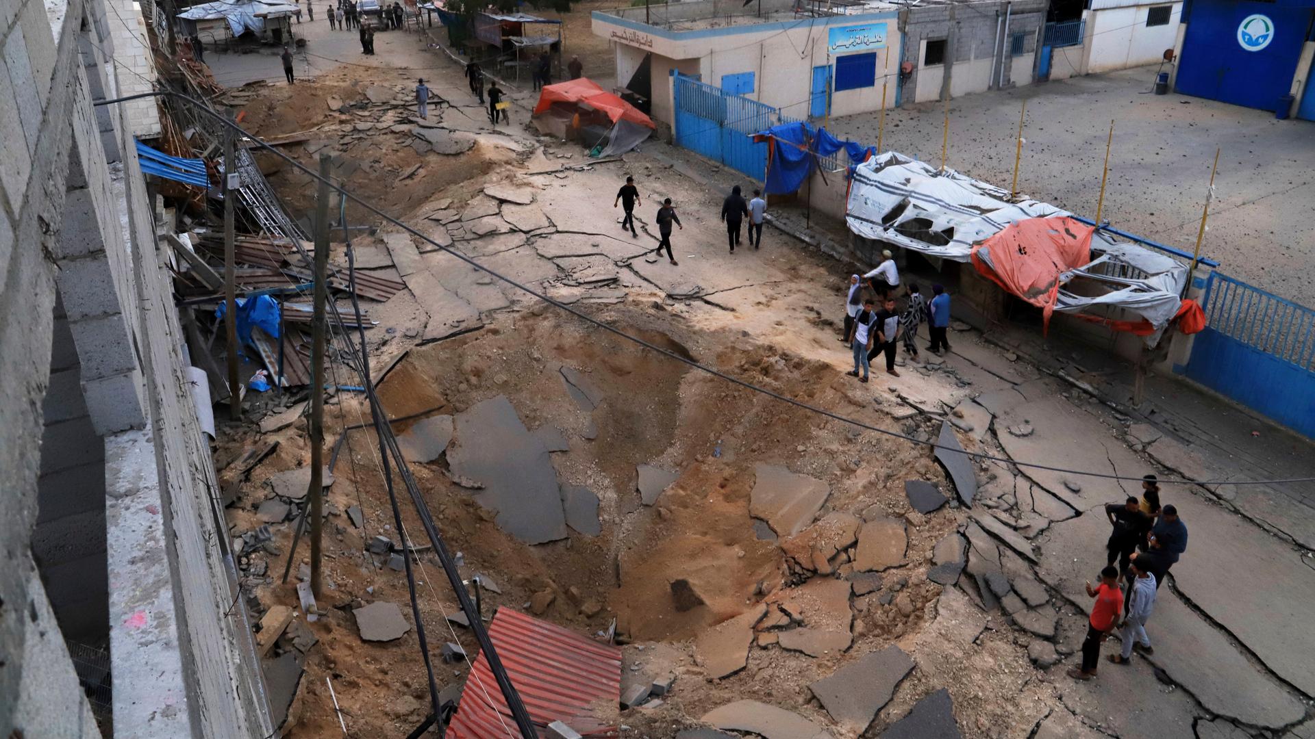  Palästinenser inspizieren den Ort eines Luftangriffs der israelischen Armee, der ein Krankenhaus in Chan Junis getroffen hat. Zu sehen ist ein Krater in einer Straße.