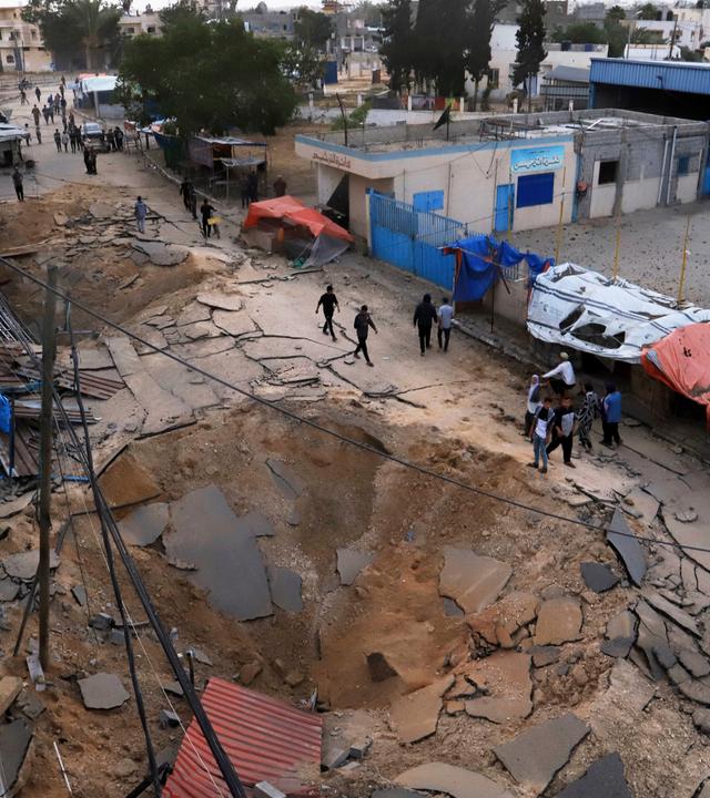  Palästinenser inspizieren den Ort eines Luftangriffs der israelischen Armee, der ein Krankenhaus in Chan Junis getroffen hat. Zu sehen ist ein Krater in einer Straße.
