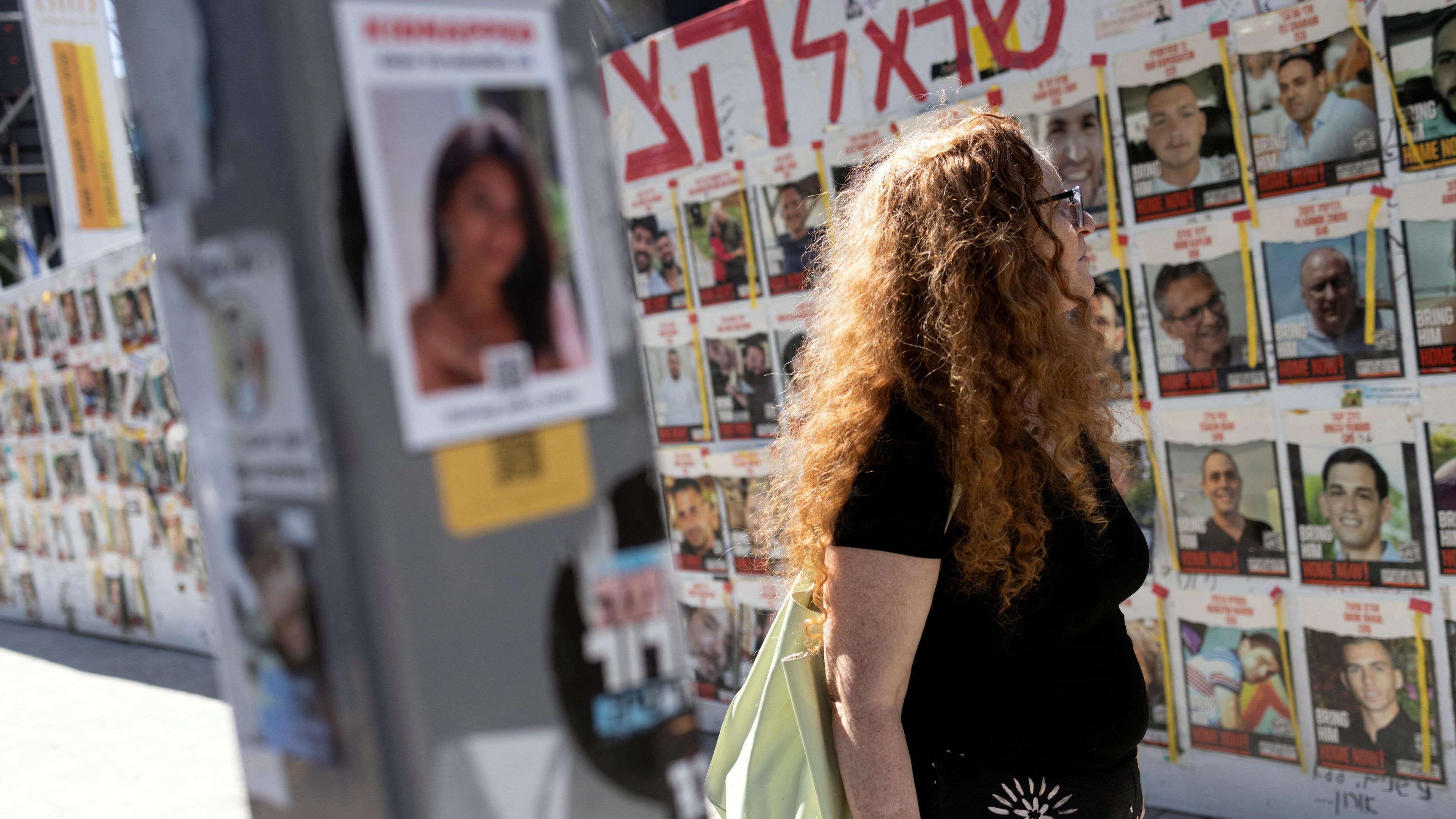 Ein Frau in Tel Aviv schaut auf eine Wand mit Bildern der Hamas-Geiseln.