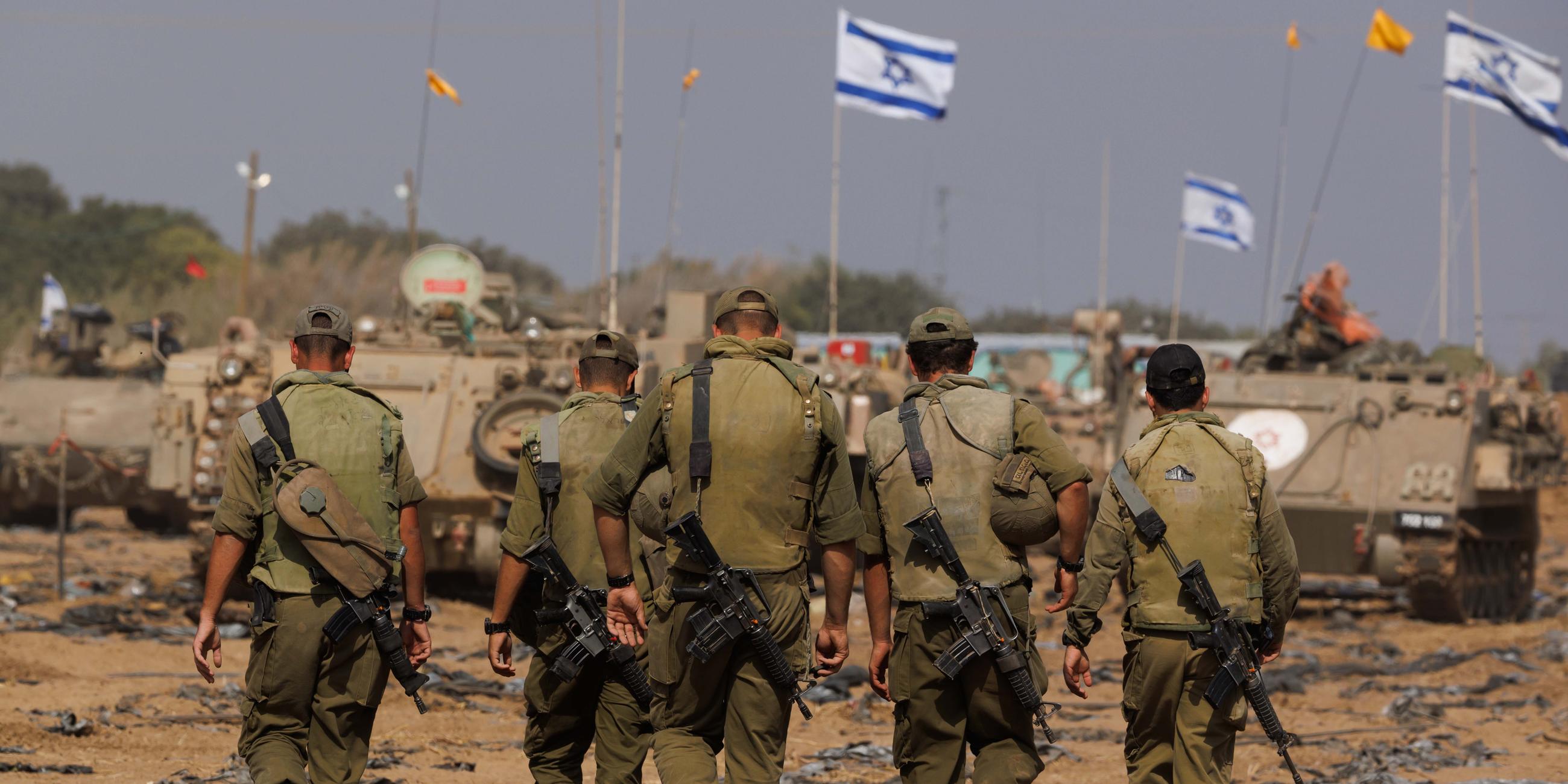 Israelische Soldaten vor Panzern an der Grenze zum Gazastreifen; im Hintergrund wehen Israel-Flaggen.