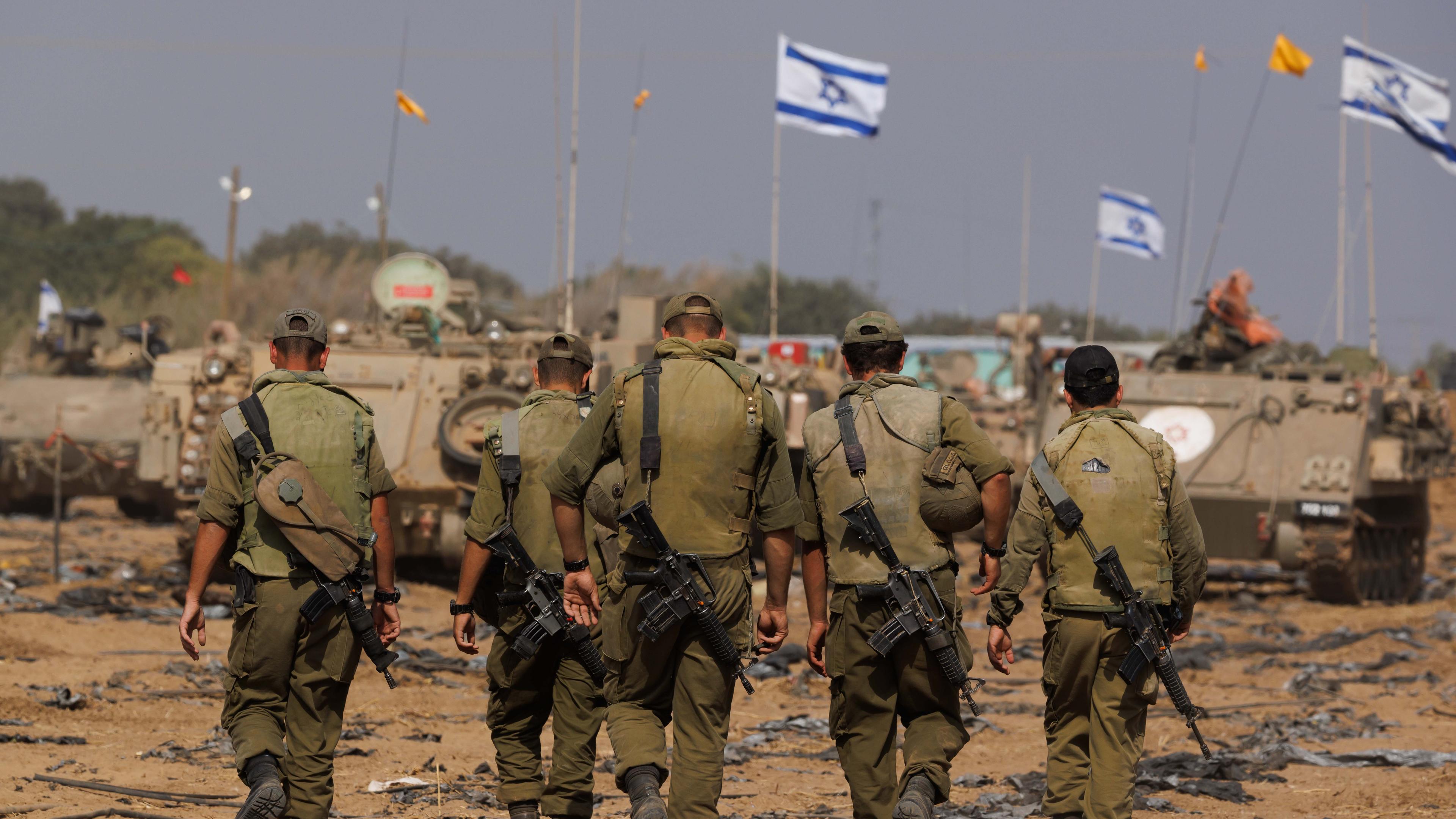 Israelische Soldaten vor Panzern an der Grenze zum Gazastreifen; im Hintergrund wehen Israel-Flaggen.