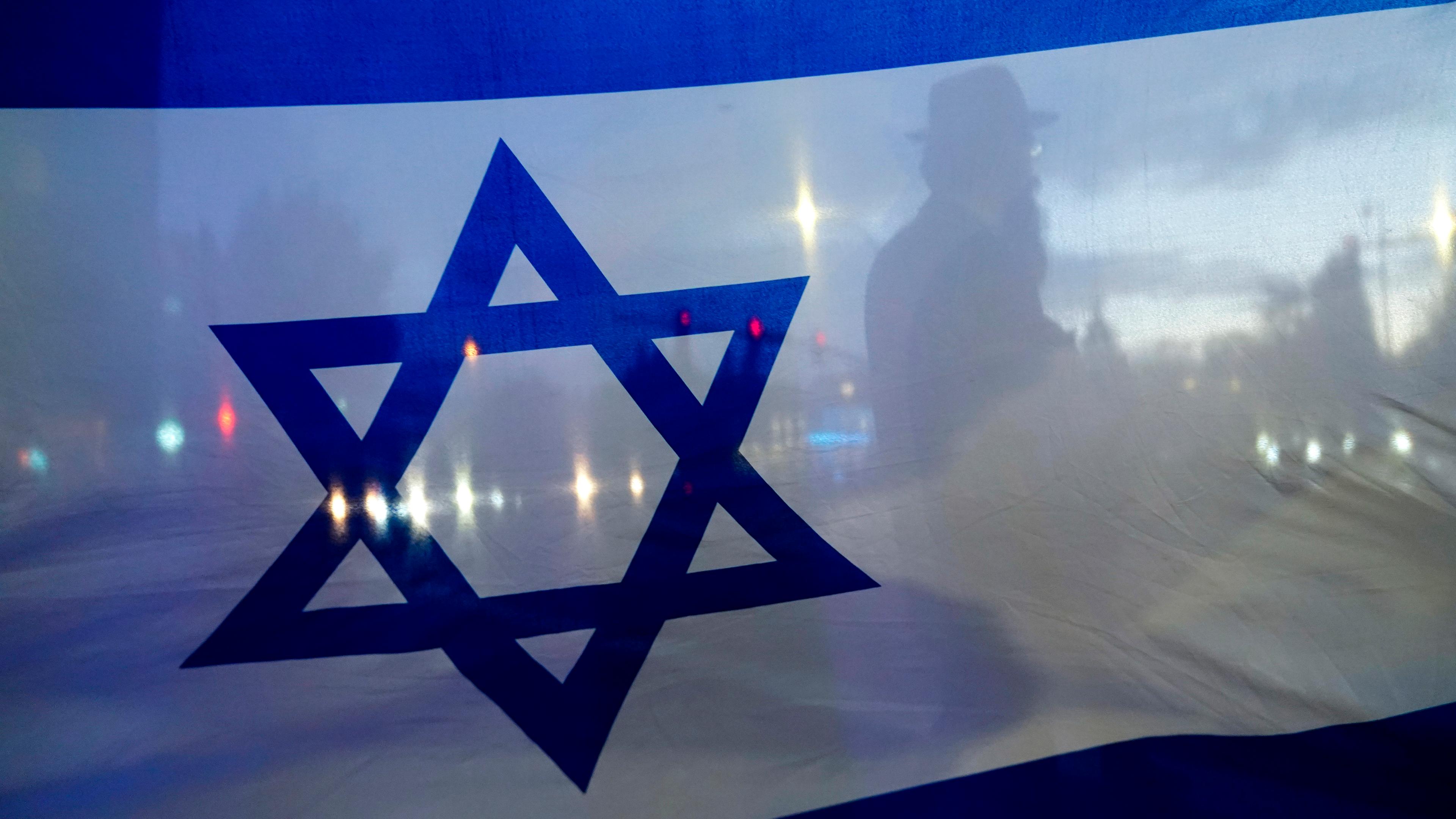 Im Vordergrund eine israelische Flagge und im Hintergrund der Straßenverkehr.