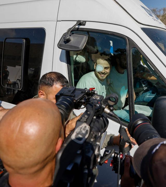 Ein weißer Transporter, in dem mehrere Männer sitzen und herausschauen wird von Kameraleuten und Fotografen belagert.