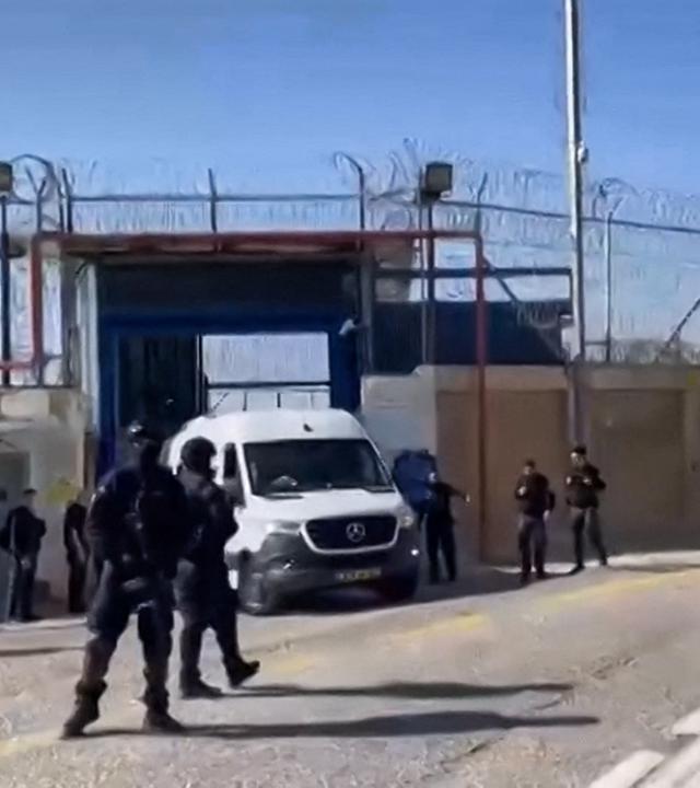 Mehrere Sicherheitskräfte stehen vor den Gefängnistoren durch die zwei Minibusse die Anlage verlassen.