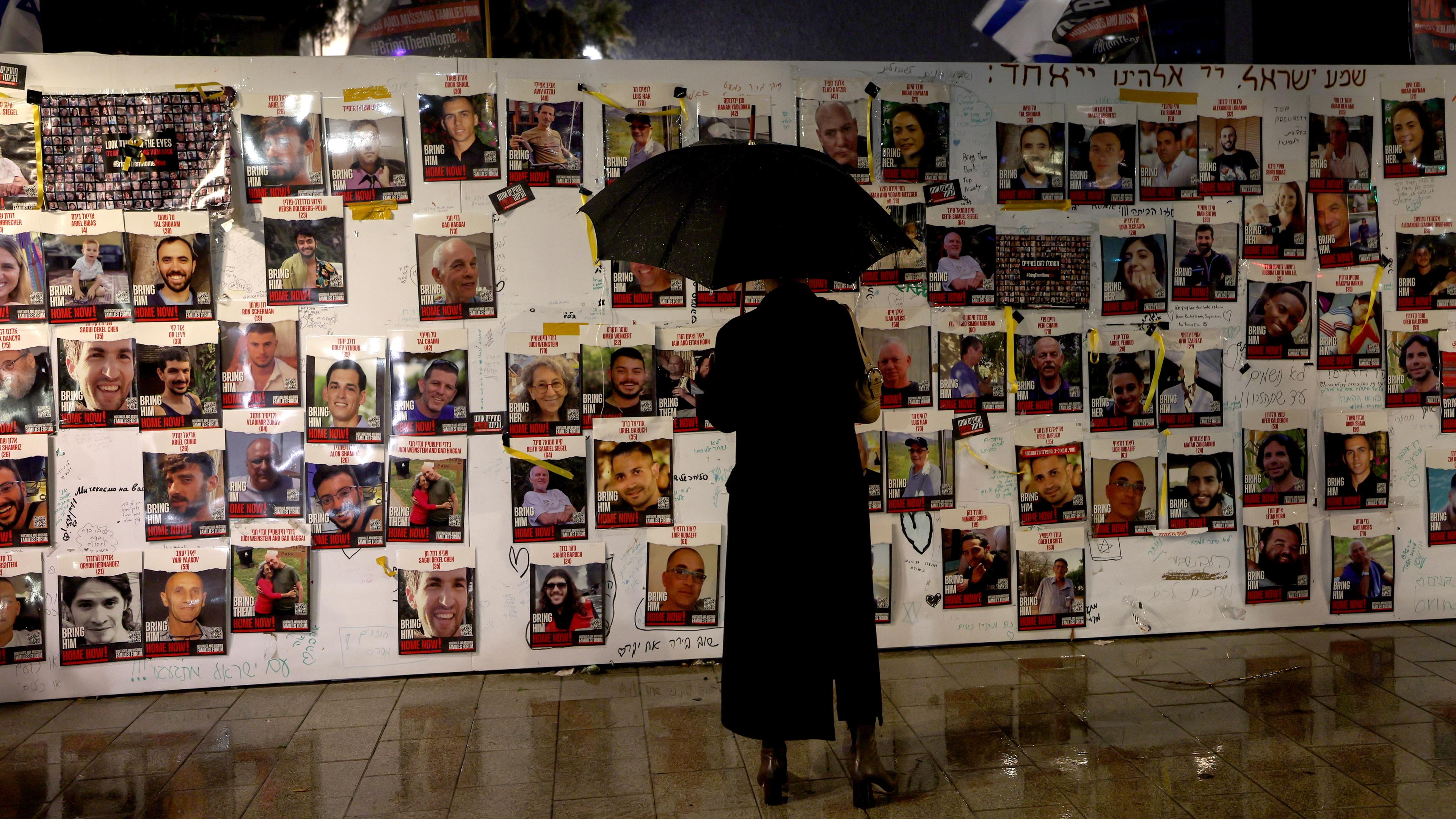 Eine Person mit Regenschirm begutachtet eine Mauer in Tel Aviv im Andenken an die nach Gaza verschleppten Geiseln.